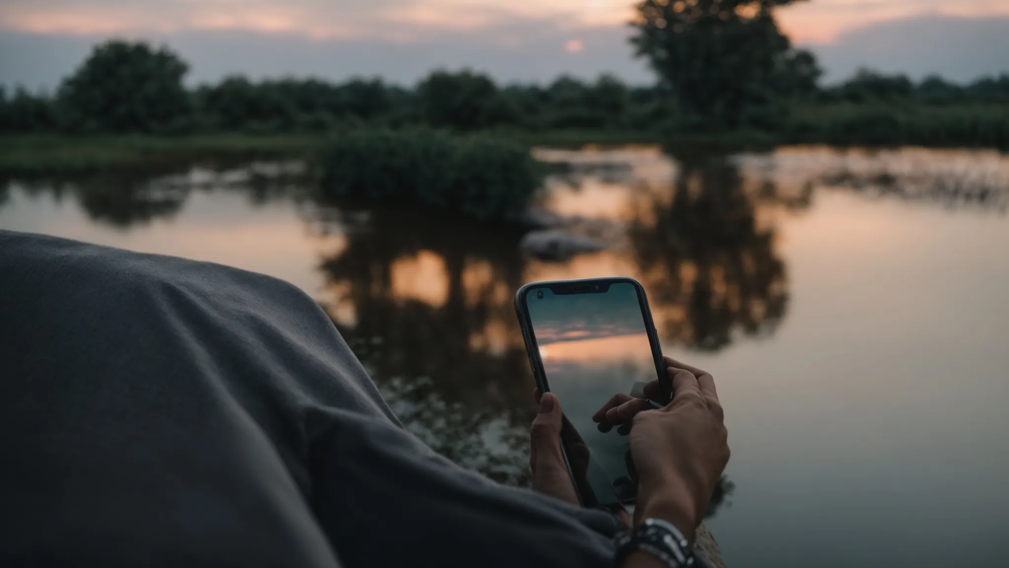 a person holding a phone, staring intently at the screen with a pond reflecting a serene sky in the background. They may be checking their voicemail or contact list.