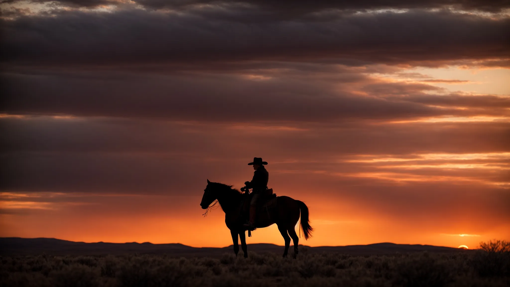 a silhouette of a cowboy on horseback against a vast, fiery sunset that paints the open western landscape.